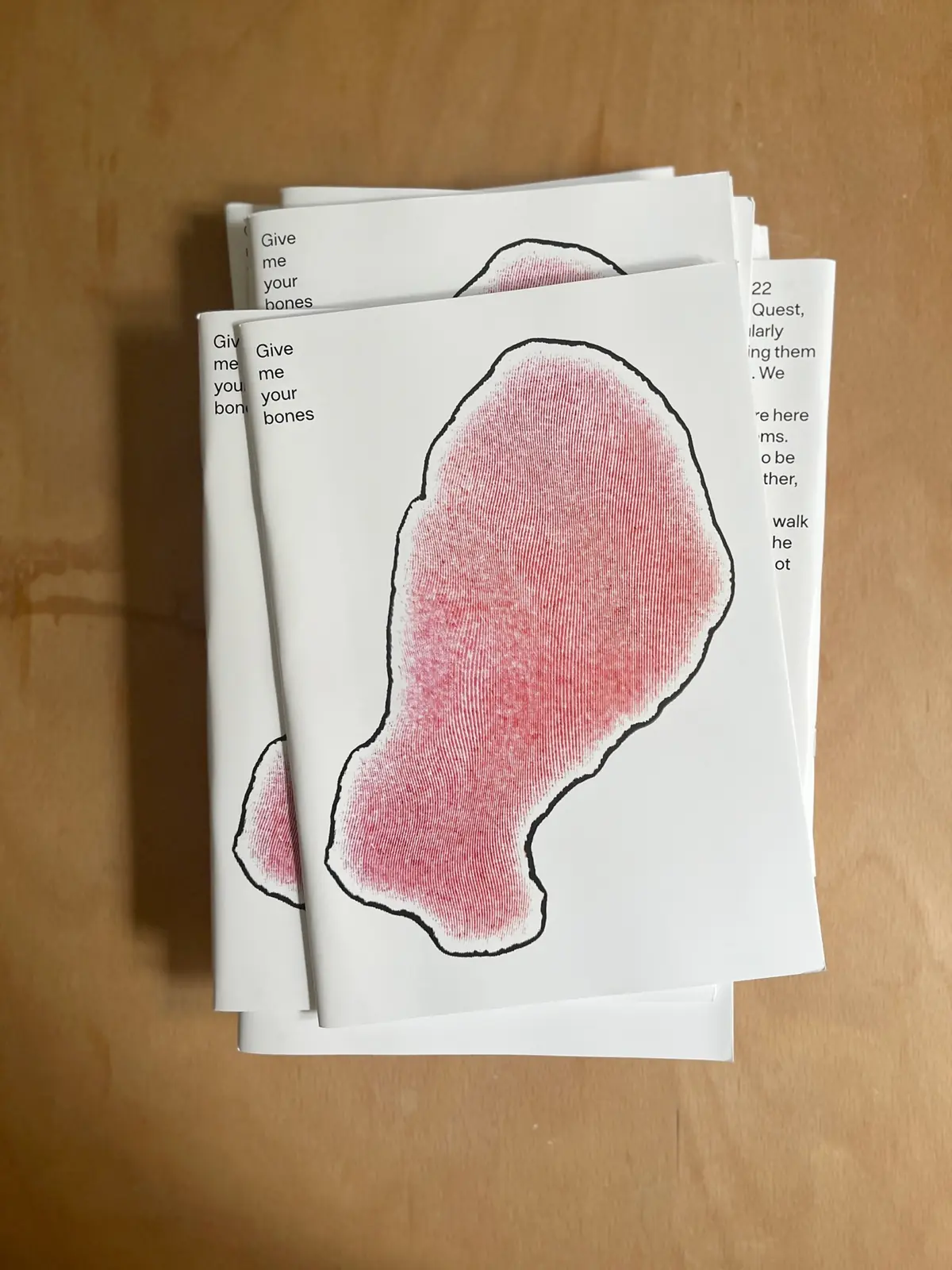 Stack of Give me your bones booklets with a red hand-drawn shape